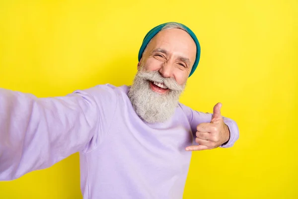 Retrato fotográfico del anciano mostrando un gesto de metal pesado riendo aislado sobre un fondo de color amarillo vivo —  Fotos de Stock