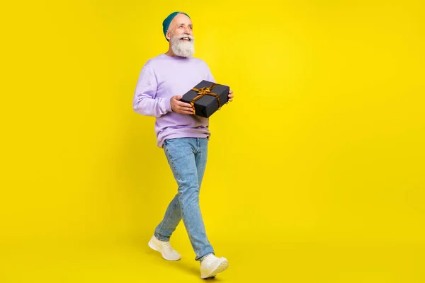 Foto di dolce eccitato uomo maturo vestito pullover viola sorridente camminare tenendo regalo scatola spazio vuoto isolato colore giallo sfondo — Foto Stock