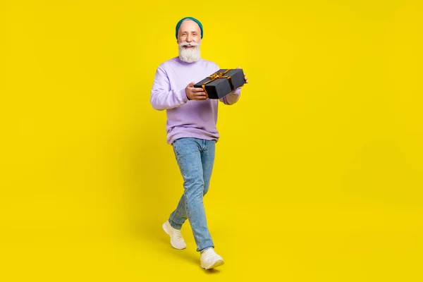 Foto de bonito atraente idade cavalheiro desgaste violeta suéter andando sorrindo segurando presente isolado cor amarela fundo — Fotografia de Stock
