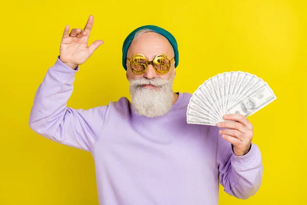Photo of funny cute age gentleman wear violet sweater headwear eyeglasses holding money dancing isolated yellow color background — Stock Photo, Image