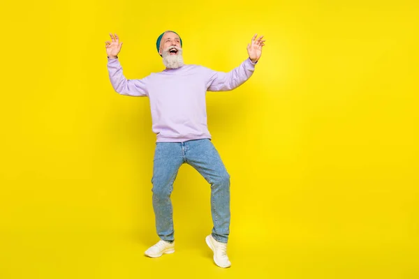 Foto de positivo funky idade cavalheiro desgaste violeta camisola headwear sorrindo dança isolado cor amarela fundo — Fotografia de Stock