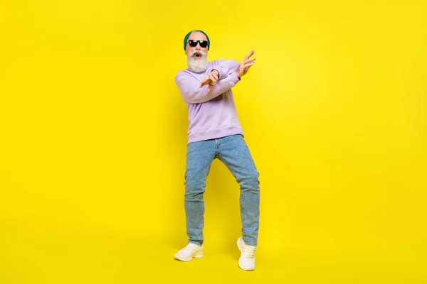 Фото позитивного досить зрілого чоловіка одягненого фіолетового пуловерного головного убору темні окуляри танцюють ізольований жовтий колір фону — стокове фото