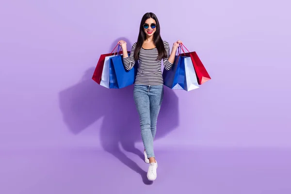 Foto de tamaño completo de la mujer sonriente feliz en gafas funky ir a pie con bolsas de compras aisladas en el fondo de color púrpura — Foto de Stock