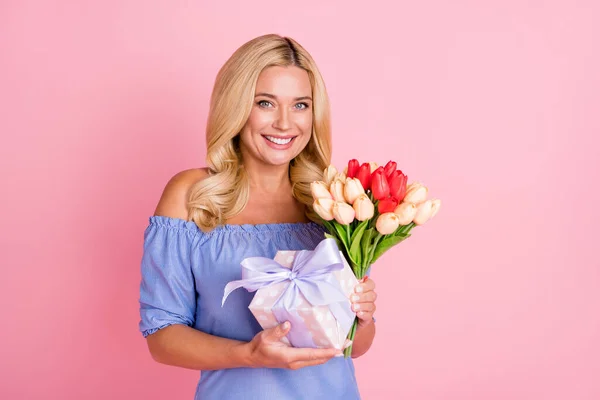 Foto de optimista rubio rizado peinado dama celebrar presente flores llevan top aislado sobre fondo de color rosa pastel — Foto de Stock