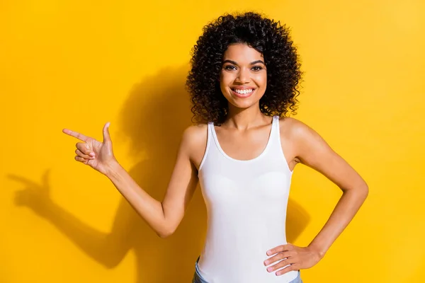 Фото счастливой афро-американки указывать пальцем пустое пространство держать руку талию изолированы на блеске желтый цвет фона — стоковое фото