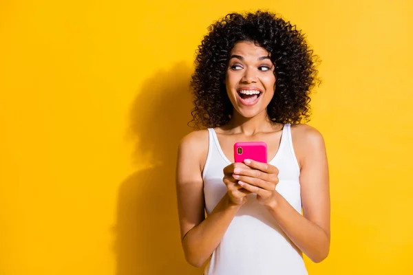 Foto de pele escura mulher de cabelos castanhos olhar espaço vazio segurar telefone desgaste branco singlet isolado no fundo de cor amarela — Fotografia de Stock