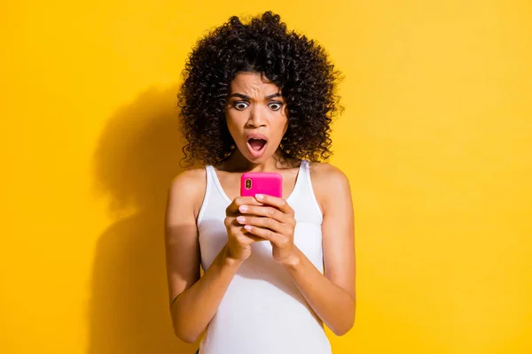 Foto de encantadora impactada joven mujer de piel oscura vestido blanco tanque-top buscando gadget moderno aislado de color amarillo de fondo — Foto de Stock