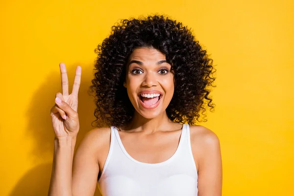 Foto de sorprendida divertida piel oscura persona boca abierta dedos muestran v-signo aislado en el fondo de color amarillo — Foto de Stock