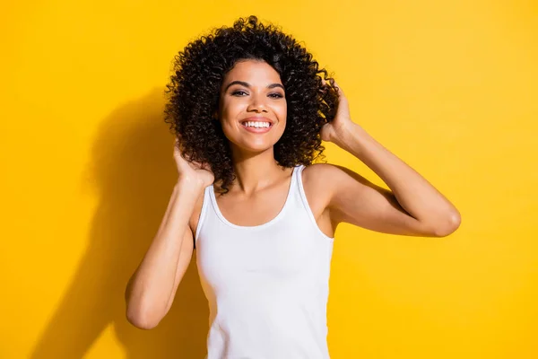Photo of adorable satisfied dark skin person hands touch wavy hairdo toothy smile isolated on yellow color background — Stock Photo, Image