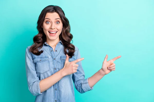 Foto de excitada joven brillante camisa de mezclilla vestida sonriendo señalando dos dedos espacio vacío color verde azulado fondo —  Fotos de Stock