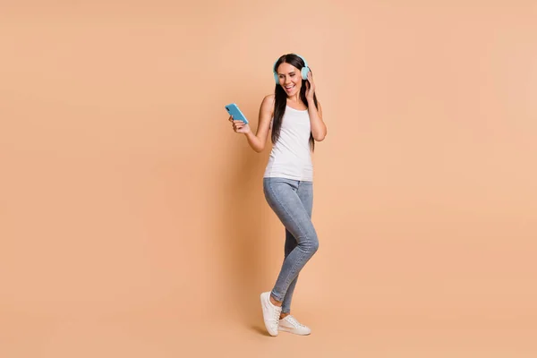 Full length foto portret van vrouw in hoofdtelefoon dansen holding telefoon in een hand geïsoleerd op pastel beige gekleurde achtergrond — Stockfoto