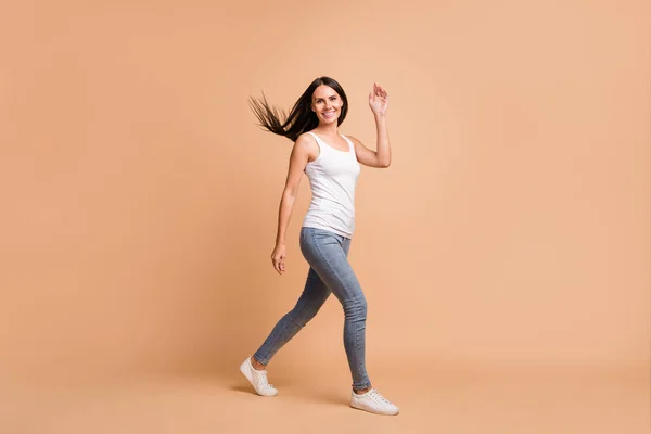 Foto de perfil de tamaño completo de la chica morena optimista go wave ropa de mano blanco top jeans zapatillas aisladas sobre fondo beige —  Fotos de Stock
