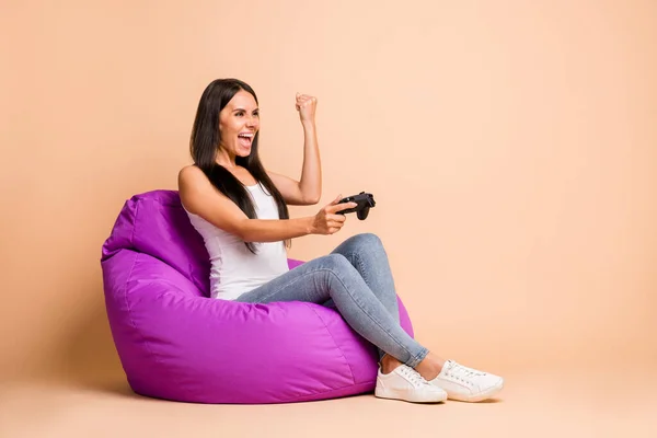 Full size zdjęcie profilu hura brunetka dziewczyna siedzieć puf z playstation pięść nosić top jeansy izolowane na beżowym tle — Zdjęcie stockowe