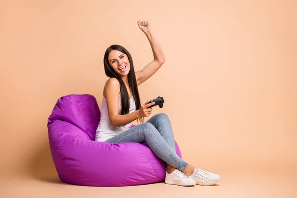 Photo portrait full body view of cheerful gamer woman holding controller sitting isolated on pastel beige colored background — Stock Photo, Image