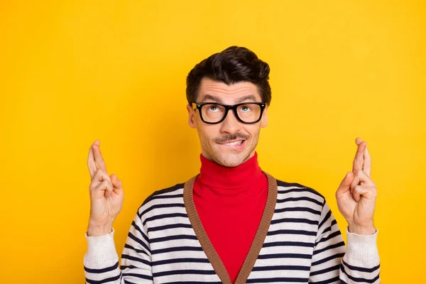 Foto van jonge man bijten lippen tanden gekruiste vingers wensen hoop bidden geluk dragen rode coltrui geïsoleerd over gele kleur achtergrond — Stockfoto