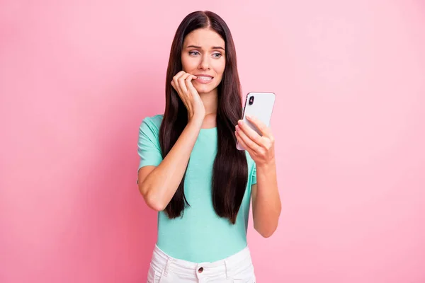 Foto van jong aantrekkelijk mooi verdrietig ongelukkig nerveus meisje bijten vingers houden smartphone geïsoleerd op roze kleur achtergrond — Stockfoto