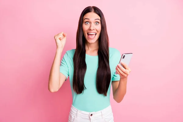 Foto de la joven hermosa feliz emocionada chica sonriente loca mantenga los puños en el teléfono de uso de la victoria aislado en el fondo de color rosa — Foto de Stock