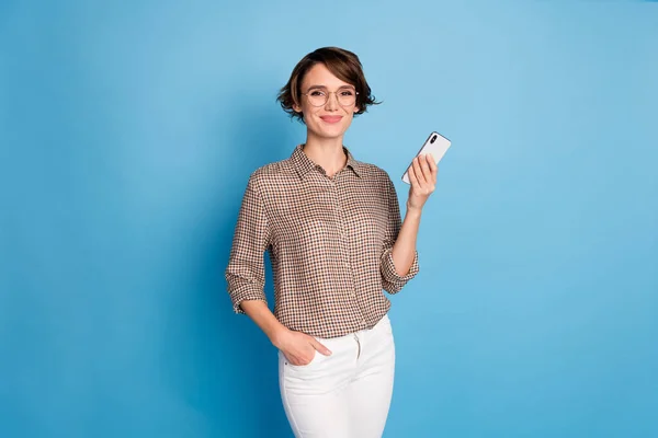 幸せな素敵な若い女性の写真は、パステルブルーの背景に隔離された手のポケットスマートフォンを保持 — ストック写真