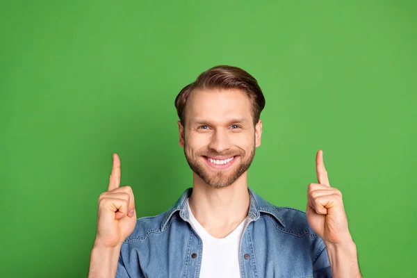 데님 셔츠를 입고 밝은 녹색 배경에 고립된 채흐느껴 웃고 있는 빈 공간을 손가락으로 가리키고 있는 남자의 사진 — 스톡 사진