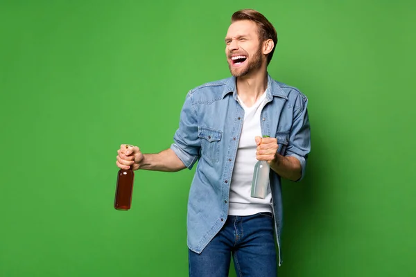 Photo portrait of laughing man keeping beer glass bottles inviting to party isolated vivid green color background copyspace — Stock Photo, Image