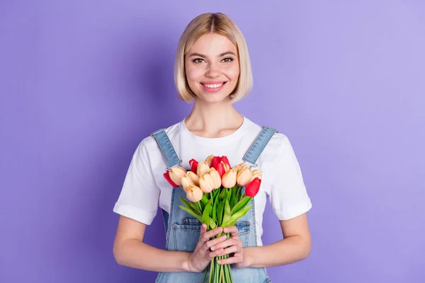 Foto de agradável otimista curto penteado loira senhora segurar flores desgaste branco t-shirt isolado no fundo violeta — Fotografia de Stock