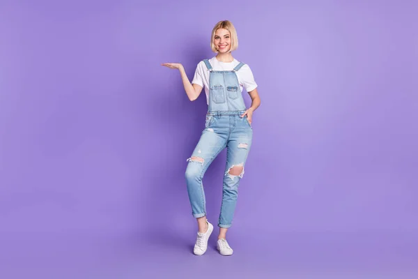 Full storlek foto av trevlig optimistisk kort frisyr blond dam hålla tomt utrymme slitage vit t-shirt övergripande isolerad på violett bakgrund — Stockfoto