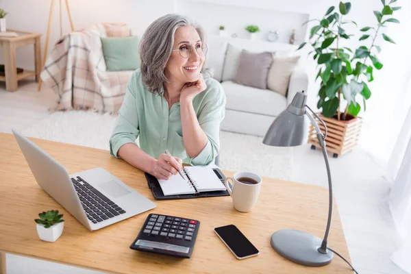 Portret van charmante vrolijke persoon zitten achter desktop hand op kin kijken geïnteresseerd tv werken vanuit huis binnen — Stockfoto