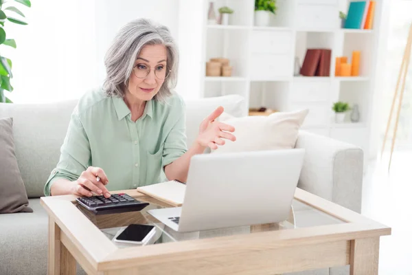 Portrait de femme concentrée sérieuse assis sur le canapé main sur calculatrice regarder ordinateur portable parler chat vidéo à l'intérieur — Photo