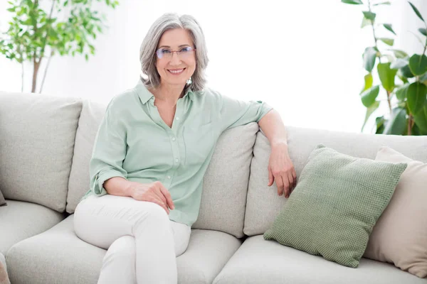 快乐快乐的老奶奶退休坐在沙发上，戴着眼镜，在屋里笑 — 图库照片