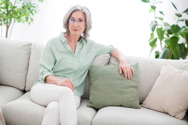 Foto de encantadora calma seria anciana sentarse sofá fin de semana usar gafas en el interior de la casa casa plana — Foto de Stock