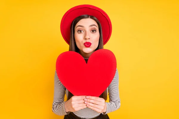 Foto de jovem menina despojado lábios enviar ar beijo coquete segurar vermelho papel coração dia dos namorados isolado sobre cor amarela fundo — Fotografia de Stock