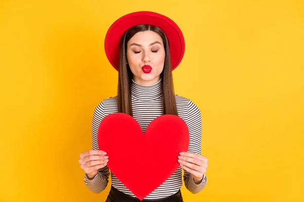 Fotografie okouzlující hezká mladá žena poslat vzduchový polibek držet velký papír srdce izolované na záři žlutá barva pozadí — Stock fotografie