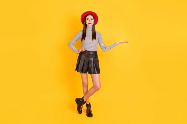 Φωτογραφία από αξιολάτρευτο λαμπερό νεαρή γυναίκα φορούν ριγέ πουκάμισο καπέλο εκμετάλλευση βραχίονα κενό χώρο απομονωμένο κίτρινο χρώμα φόντο — Φωτογραφία Αρχείου