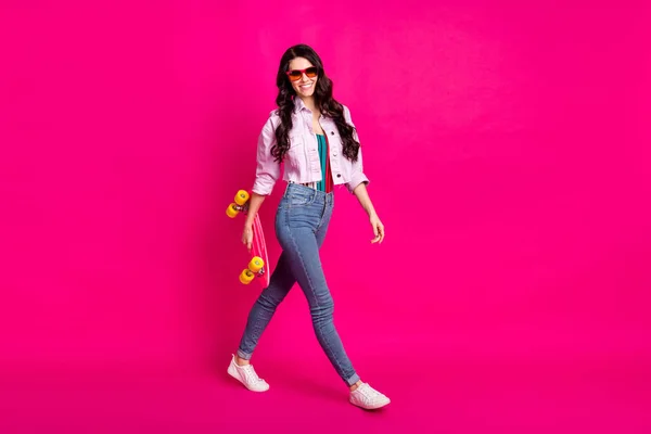Full storlek profil foto av optimistisk brunett trevlig dam gå hålla skridsko slitage jacka jeans sneakers isolerade på rosa färg bakgrund — Stockfoto