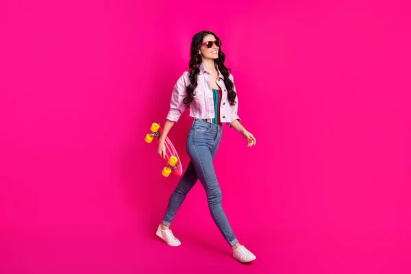 Full storlek profil sida foto av unga vackra cool säker flicka gå promenad med skateboard isolerad på rosa färg bakgrund — Stockfoto
