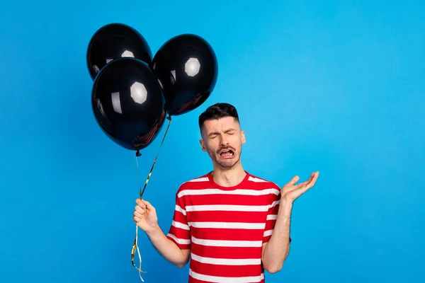 Foto de infeliz infeliz joven llorar mantenga globos molestos en cumpleaños aislado en el fondo de color azul —  Fotos de Stock