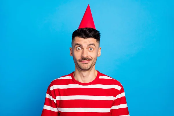 Foto de divertido incómodo joven usar cono de cumpleaños día alegre aislado sobre fondo de color azul pastel — Foto de Stock