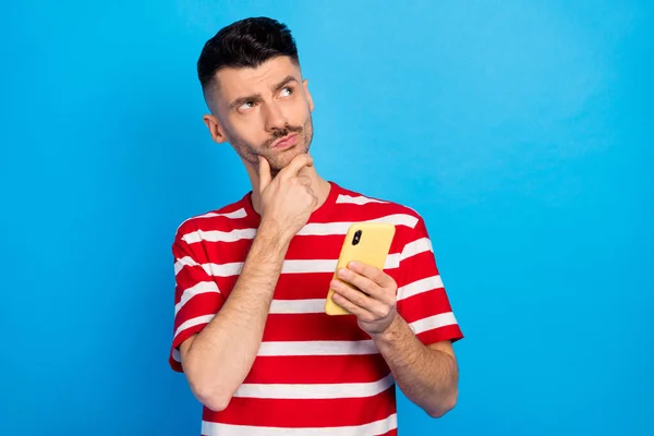 Foto de encantador chico joven reflexivo mirada espacio vacío imaginar comentario sostener la barbilla de la mano del teléfono aislado sobre fondo de color azul —  Fotos de Stock