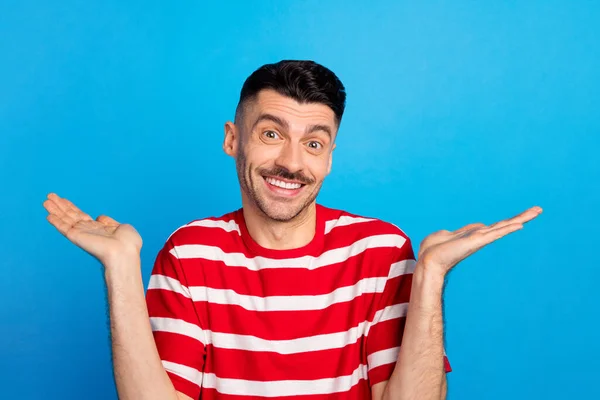 Foto de engraçado confundido jovem desgaste listrado t-shirt crescente braços isolado azul cor fundo — Fotografia de Stock