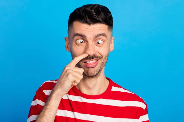 Foto de divertido tonto joven feliz hombre recoger la nariz hacer funky cara aislado en pastel fondo de color azul — Foto de Stock