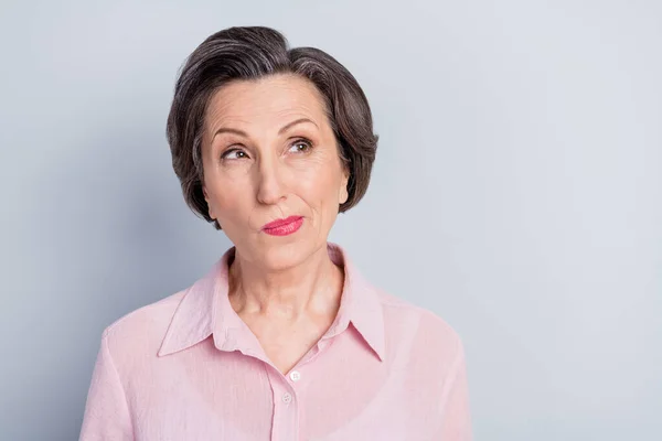 Foto de señora madura linda dudosa usar ropa rosa sonriendo buscando espacio vacío aislado fondo de color gris — Foto de Stock