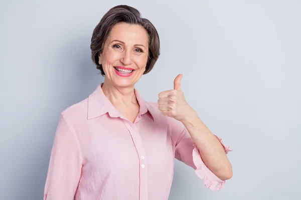 Photo de douce charmante femme d'âge habillé chemise rose souriant montrant pouce vers le haut espace vide isolé fond de couleur grise — Photo