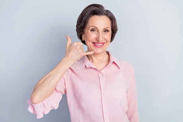 Portret atrakcyjnej emerytowanej wesołej kobiety pokazując zadzwoń do mnie znak komórkowy izolowany na szarym pastelowym tle koloru — Zdjęcie stockowe