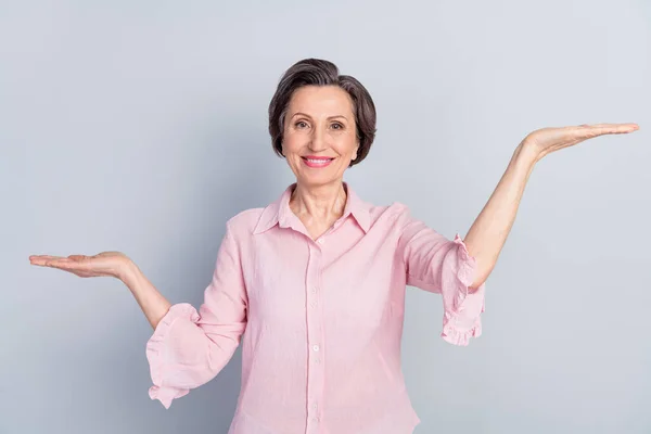 Foto de alegre mulher velha feliz segurar as mãos espaço vazio balanças produto isolado no fundo de cor cinza — Fotografia de Stock