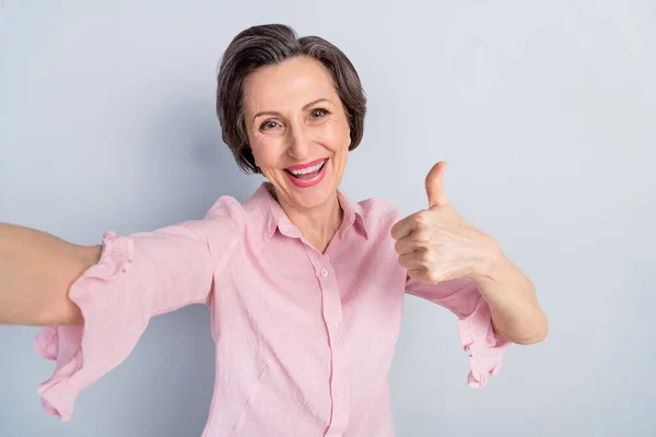 迷人的老年心情愉快的女人的自画像，在灰色的彩色背景上表现出大拇指突起广告 — 图库照片