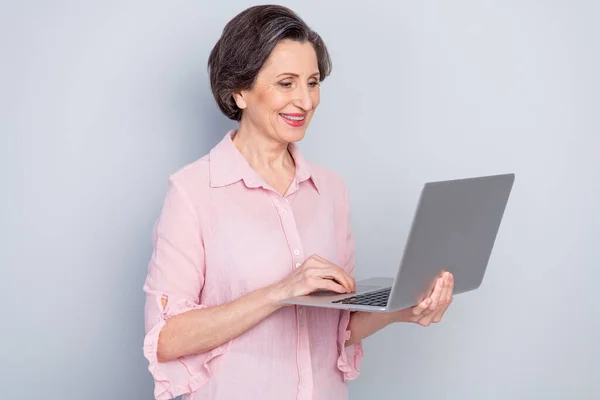 Photo of pretty charming age woman dressed pink shirt smiling typing modern device isolated grey color background — Stock Photo, Image