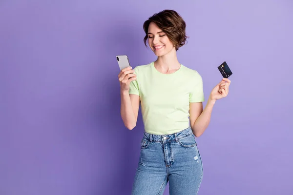 Portré szép vidám lány gazdaság a kezében bankkártya segítségével szerkentyű bolt internetes böngészés elszigetelt felett ibolya színű háttér — Stock Fotó