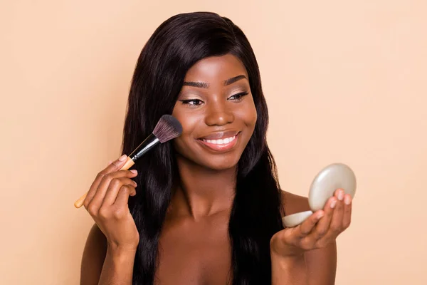 Portrait of attractive cheerful shine girl applying powder on cheek preparing isolated over beige pastel color background