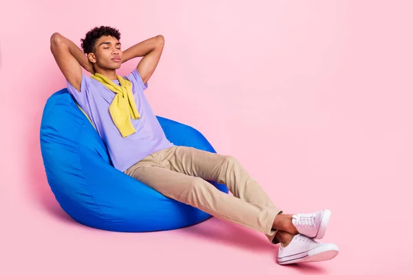 Profilo completo del corpo foto laterale di giovane ragazzo nero sedersi fagioli sedia resto rilassare dormire braccia dietro mano isolato su sfondo di colore rosa — Foto Stock