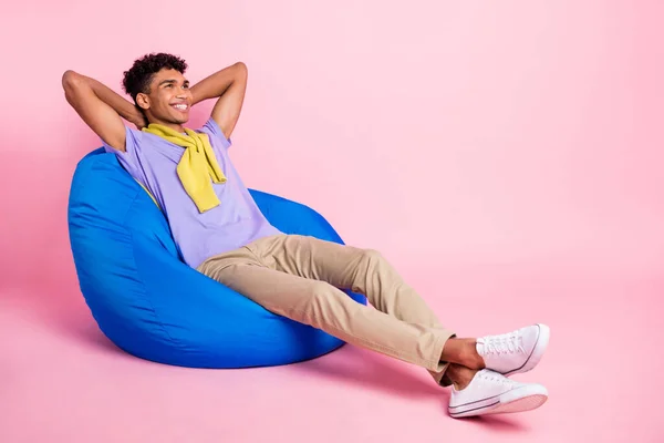 Full body profile side photo of young afro man happy rest chair hands behind head look empty space isolated over pastel color background